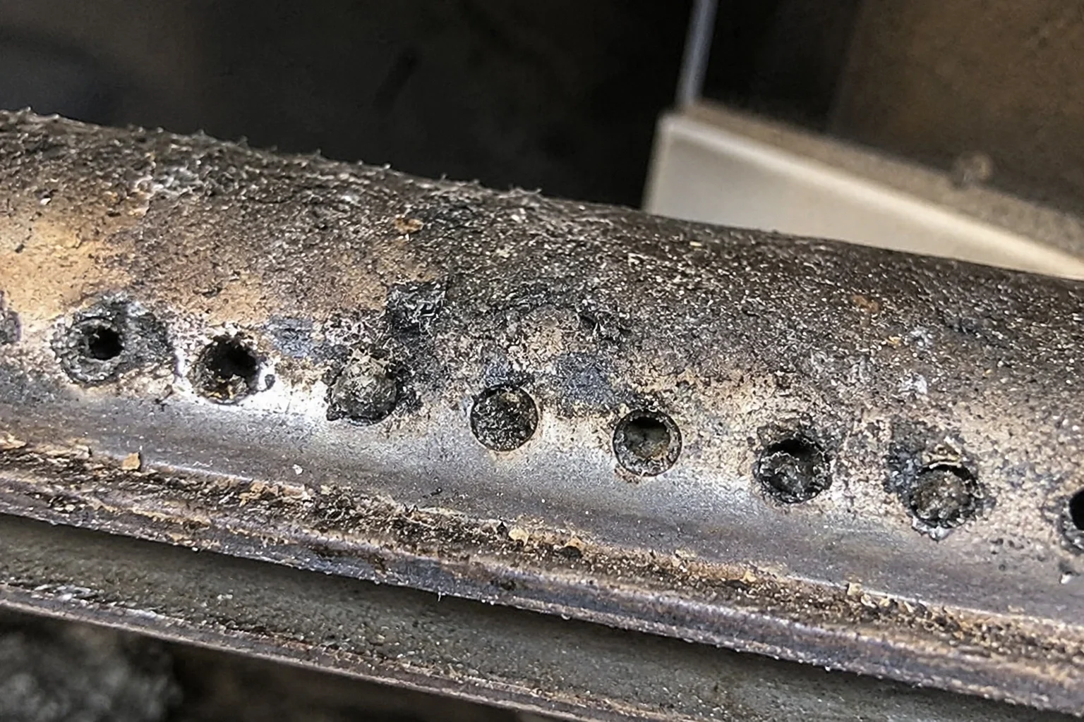 Close-up of clogged gas fireplace burner ports causing a weak flame