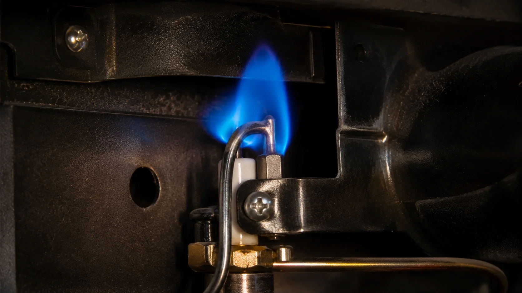 Close-up of gas fireplace pilot light inspection showing healthy blue flame
