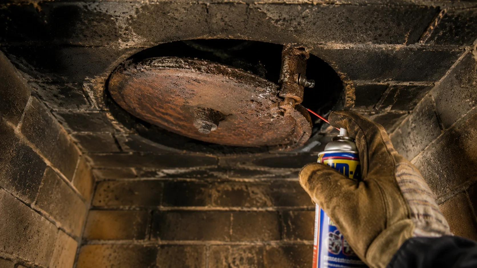 A rusty fireplace damper stuck in a partially closed position inside a chimney
